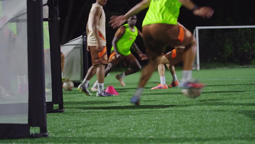A low-angle view of a soccer player's skilled footwork as they dribble past defenders and score a goal during a night practice session