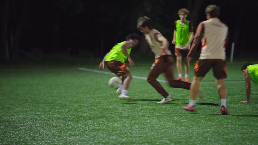Dynamic slow-motion tracking shot of young men playing a competitive game of soccer on a lit turf field at night