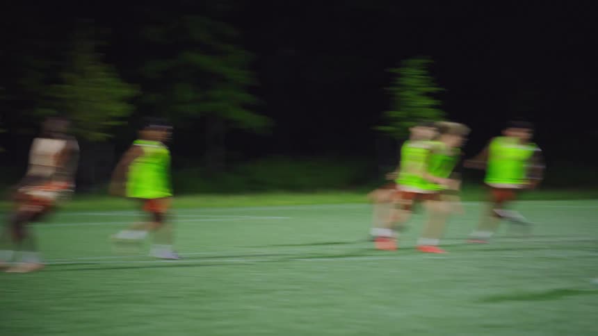 In a dramatic slow-motion sequence, a soccer team skillfully advances the ball down a lit field at night, culminating in a powerful goal