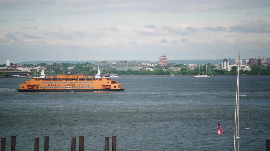 The iconic orange Staten Island Ferry sails across the New York Harbor on a cloudy day