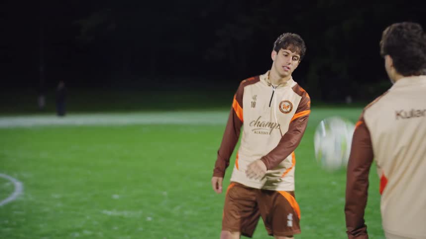 Diverse soccer teammates skillfully pass and juggle a ball between them during a nighttime practice session on a brightly lit field