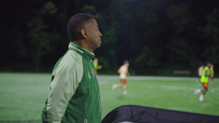 A dedicated soccer coach observes his team's practice on a lighted field at night
