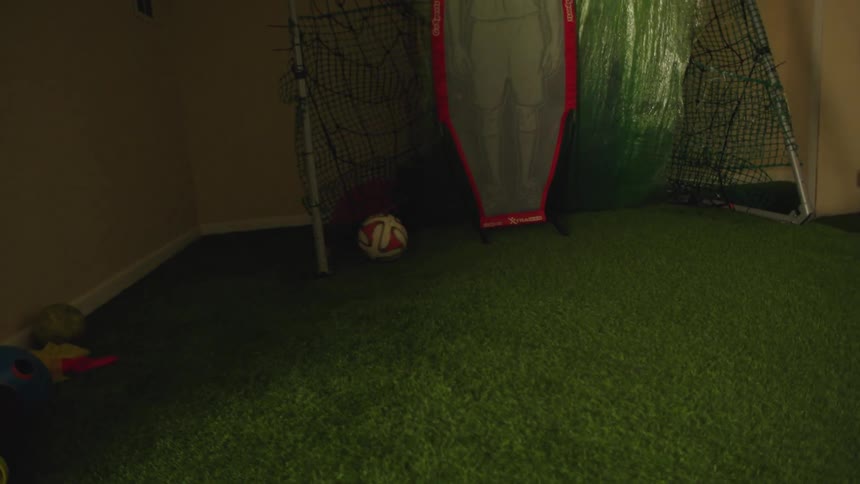 A soccer player's feet dribble a ball before he kicks it into a goal and walks forward in an indoor training room