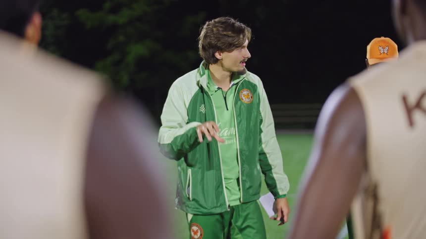 A dedicated soccer coach passionately instructs his team during a huddle on the pitch at a night training session