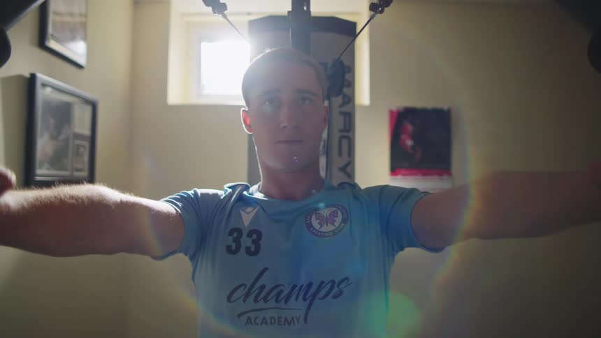 Determined young man with a lip piercing works out on a chest fly machine in a sunlit home gym, looking into the camera