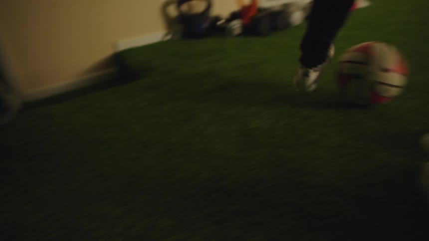 A dedicated young soccer player performs dribbling drills with a ball and cones on an indoor artificial turf field