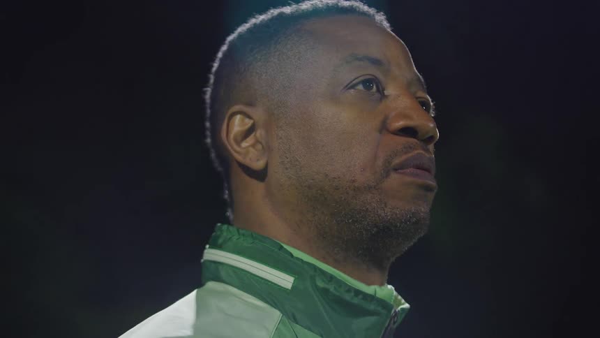 Low-angle profile shot of a focused African American coach standing under a light at night