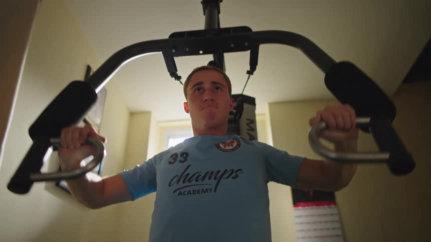 A focused athletic man performs a chest fly workout on a home gym machine, filmed from a low angle