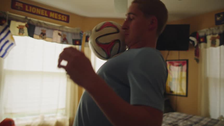 A young soccer enthusiast skillfully practices juggling and balancing a soccer ball in his bedroom in slow motion