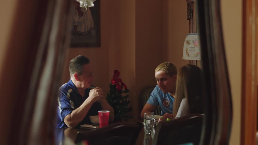 A candid reflection of a father and his two teenage children talking during a family meal at the dining table