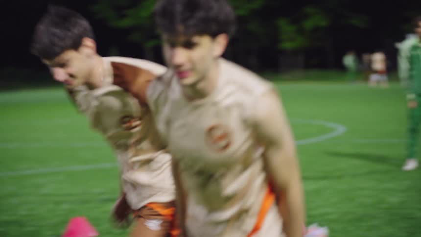 A soccer coach leads his team through various agility and running drills during a night practice on a brightly lit field
