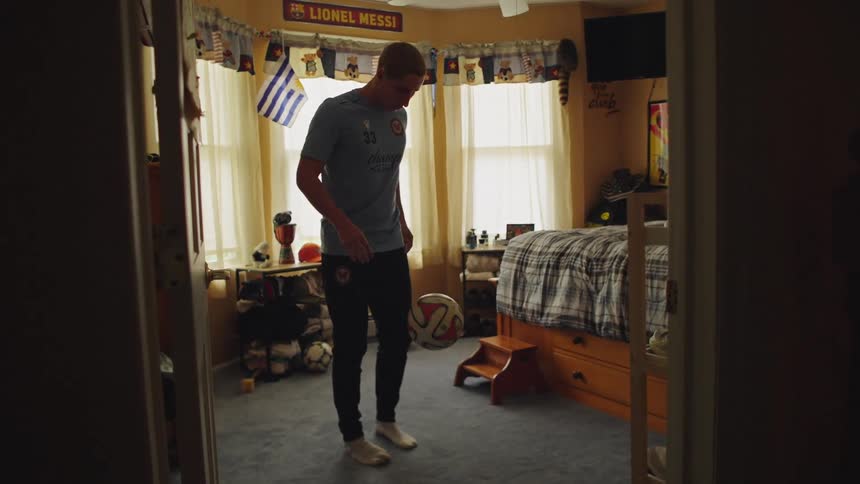 A young soccer player skillfully juggles a soccer ball in slow motion inside his sports-themed bedroom