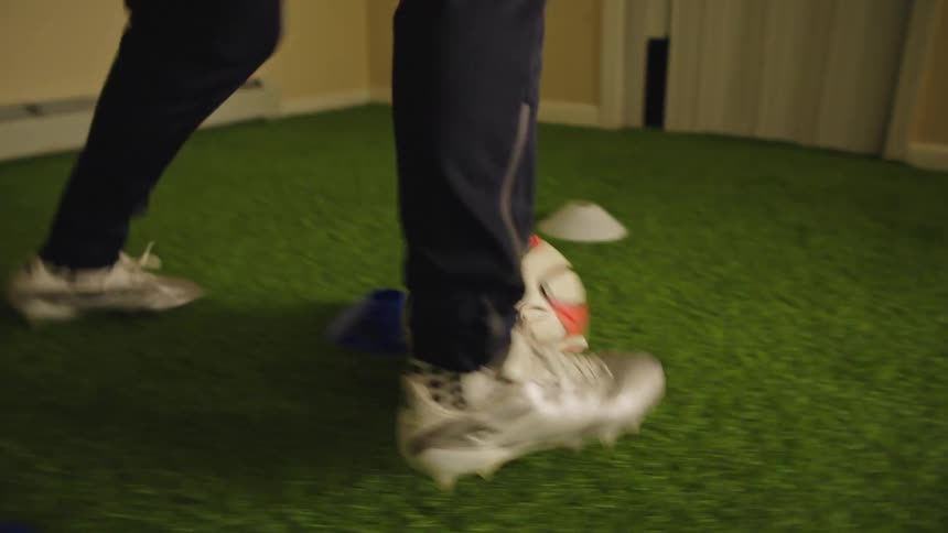A young soccer player practices his dribbling skills and footwork around training cones on an indoor artificial turf field