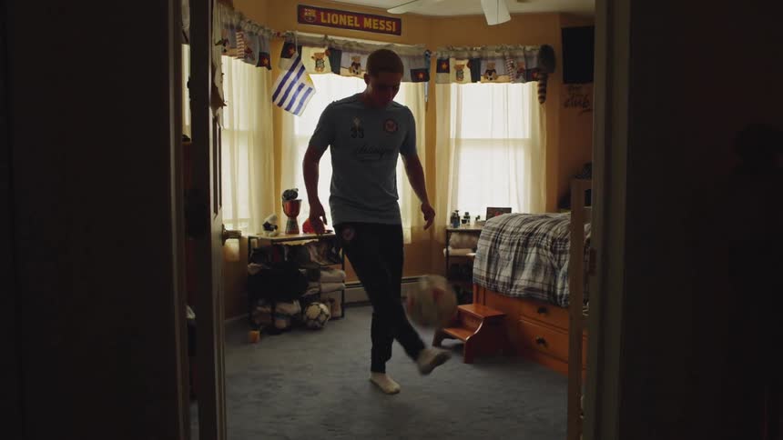 Talented young soccer player practices his juggling skills in slow motion inside his sports-themed bedroom