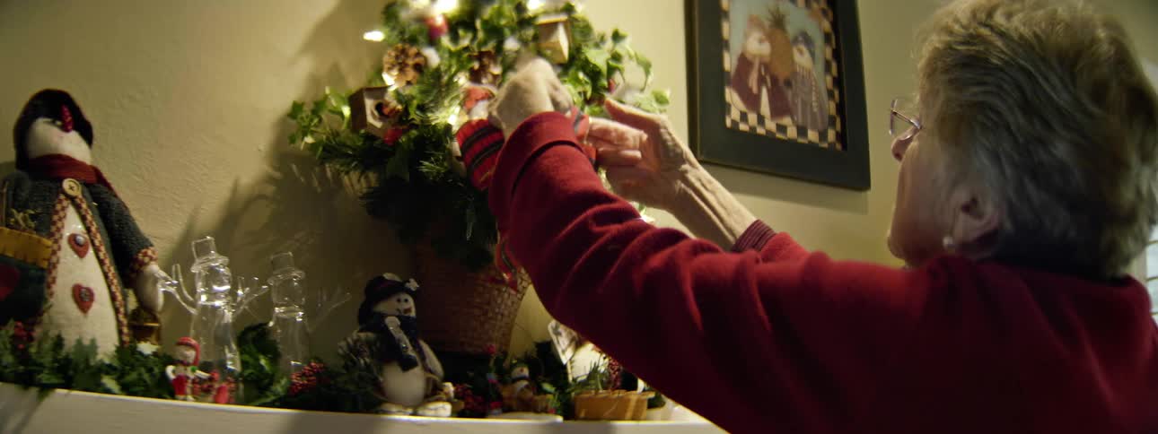 A woman straightens a wreath above a chimney