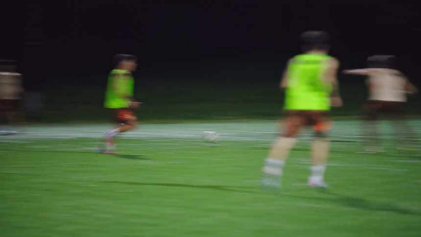 Slow motion footage captures a group of young men playing a competitive soccer match on an illuminated field at night