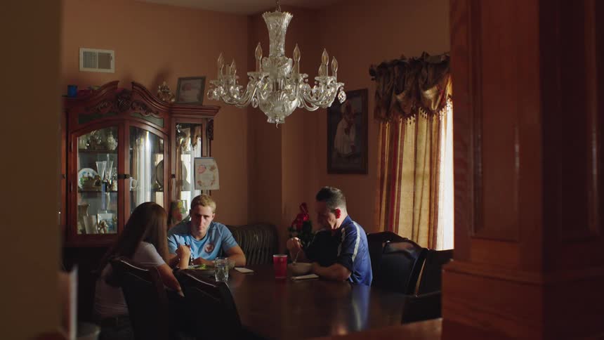 A father and his two young adult children share a happy conversation while eating a meal together in their sunlit dining room