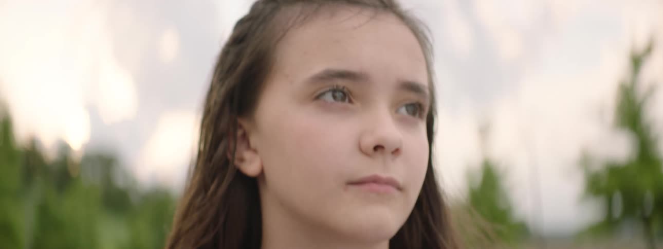 Close up slow rack focus on the serious and thoughtful face of a young girl with brown hair outdoors