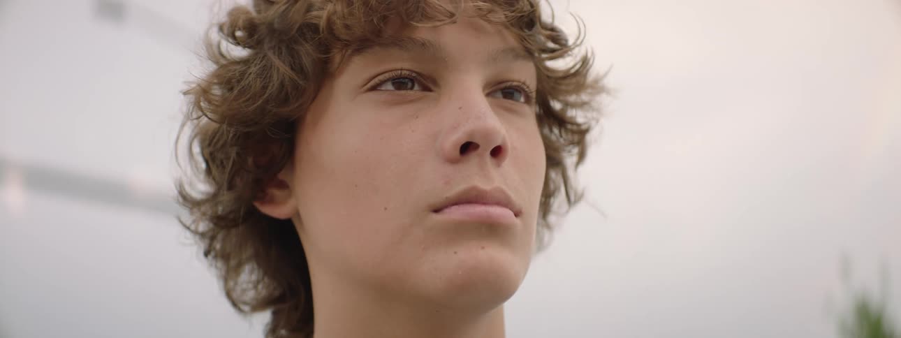 Close-up slow motion of a determined young boy with curly hair staring intently at something off-camera