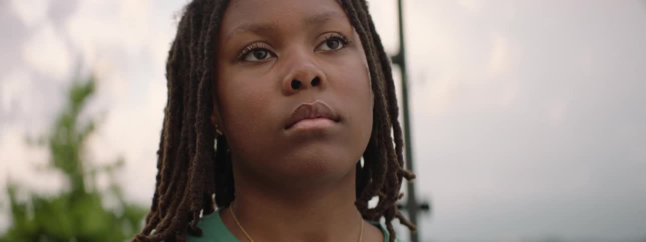A powerful close-up portrait of a young Black person with locs looking up thoughtfully on a cloudy day