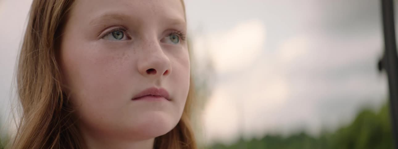 A slow focus pull reveals a close-up of a pensive young girl with red hair and freckles looking off into the distance
