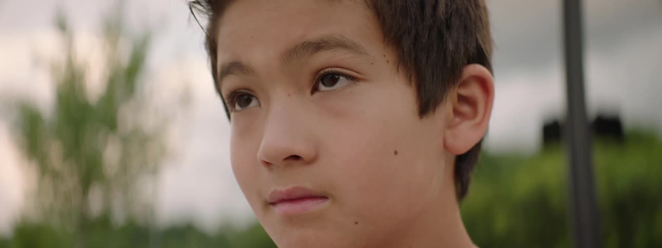 A thoughtful young boy looks off into the distance as the camera slowly comes into focus on his face