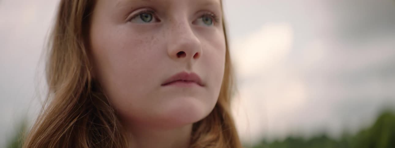 A slow focus pull reveals the thoughtful, serious face of a young girl with freckles and light eyes as she looks off-camera