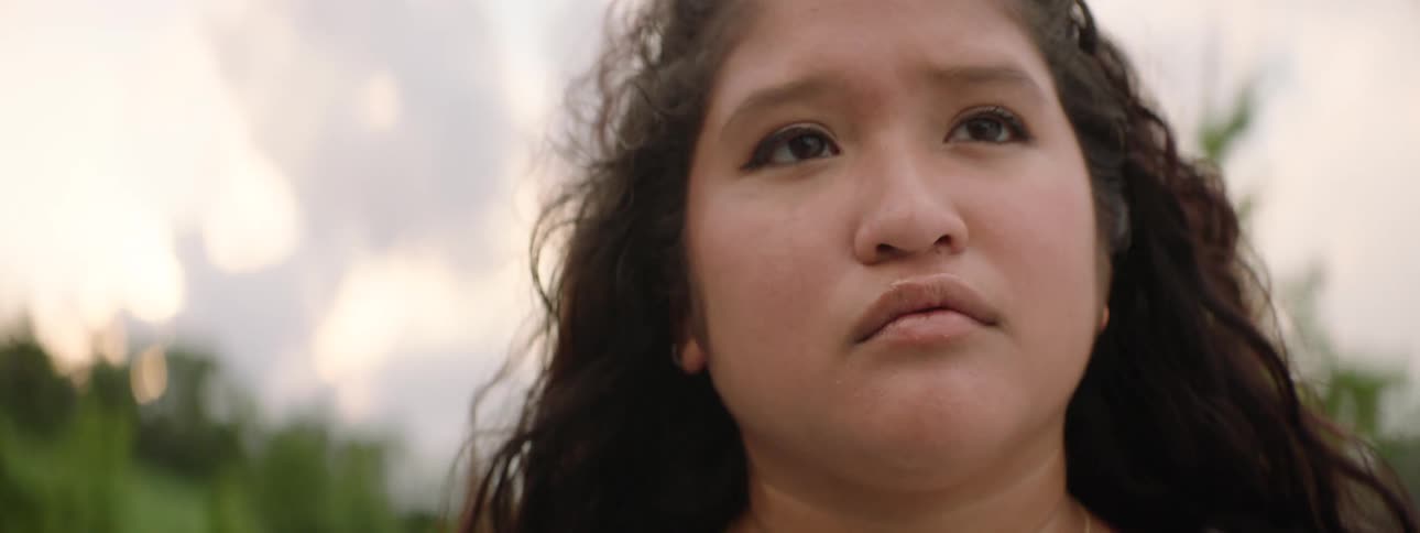 A low-angle close-up shot of a young woman with a determined expression looking up towards the sky