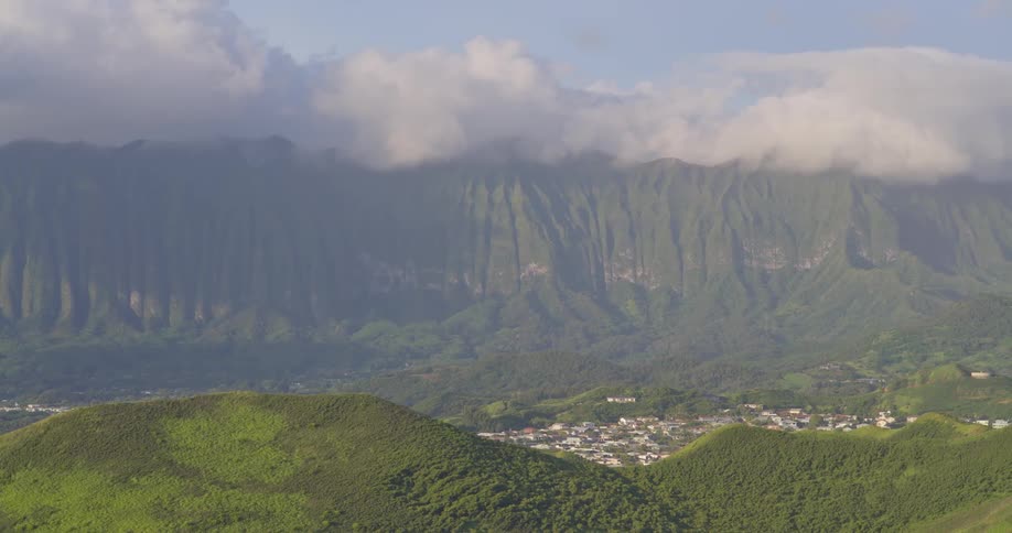 A slow zoom out reveals a vast green valley with a small town at the foot of a majestic, cloud-covered mountain range