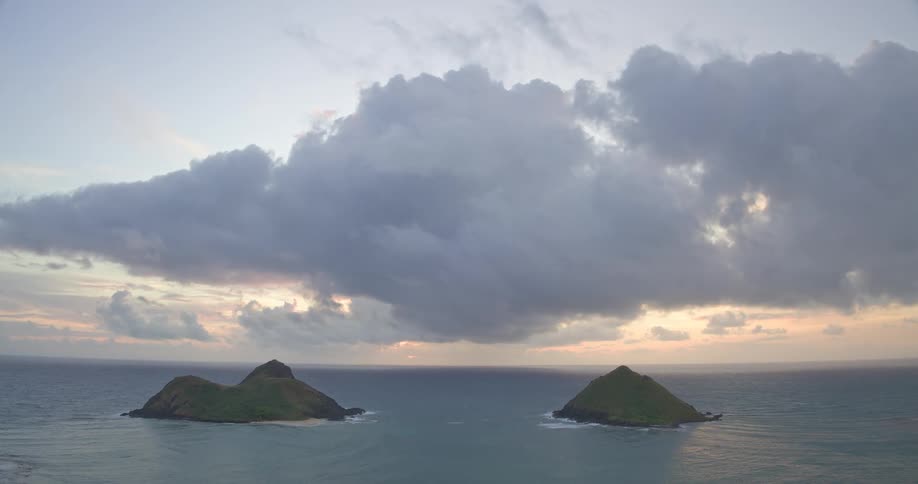 A dramatic cloudy sky looms over two tranquil tropical islands in the vast ocean during a beautiful sunrise