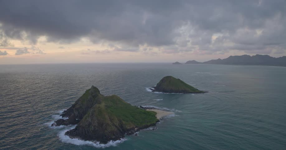 A wide, scenic view of the Mokulua Islands off the coast of Oahu, Hawaii, during a cloudy sunrise