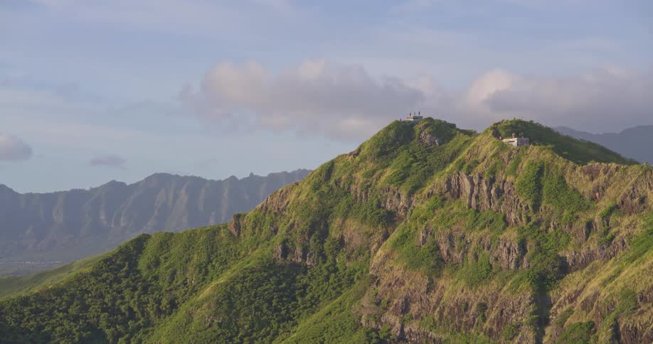 A slow zoom out reveals a scenic hiking trail with pillbox bunkers atop a lush green mountain ridge in Oahu, Hawaii