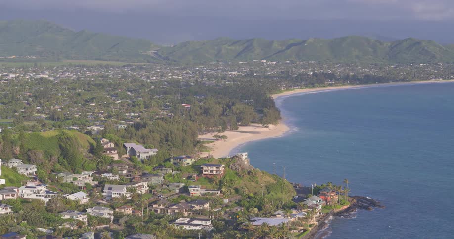 An expansive view of a Hawaiian coastal community, where lush green hills meet the turquoise waters of a tranquil bay