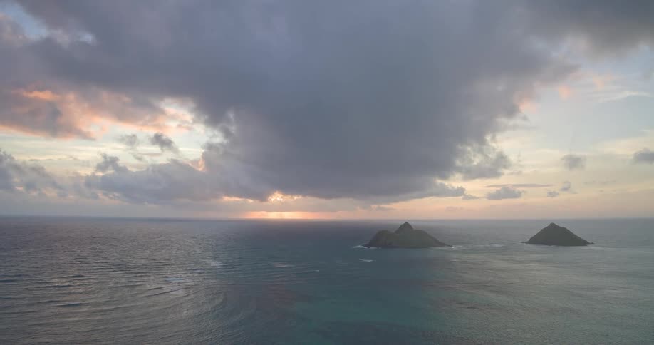 A beautiful aerial view pulls back to reveal a dramatic and cloudy sunrise over the ocean with two small islands