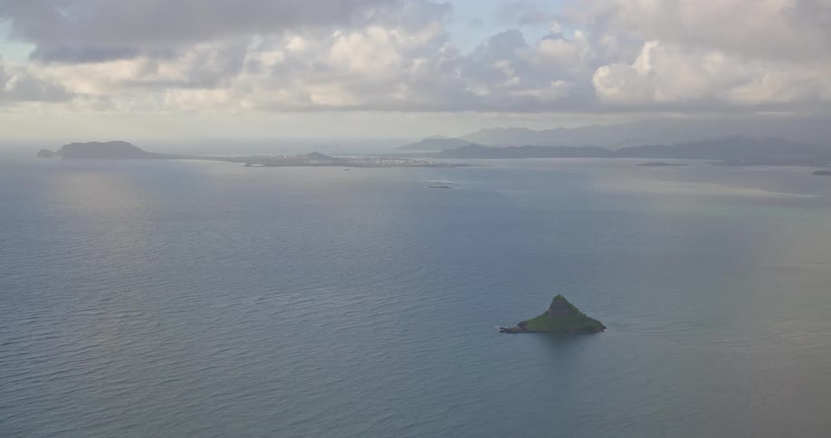 A wide, static shot captures the famous Chinaman's Hat island off the coast of Oahu, Hawaii, on a calm, cloudy day
