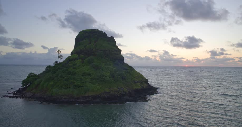 A serene aerial view captures a lush tropical island surrounded by the calm ocean at sunrise