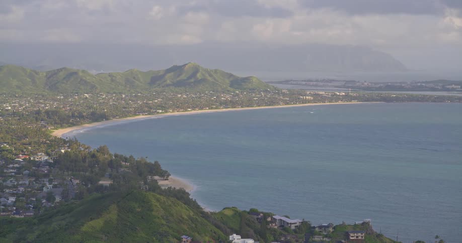 A wide scenic shot of Kailua Bay on the island of Oahu, Hawaii, shows the lush green coastline and town