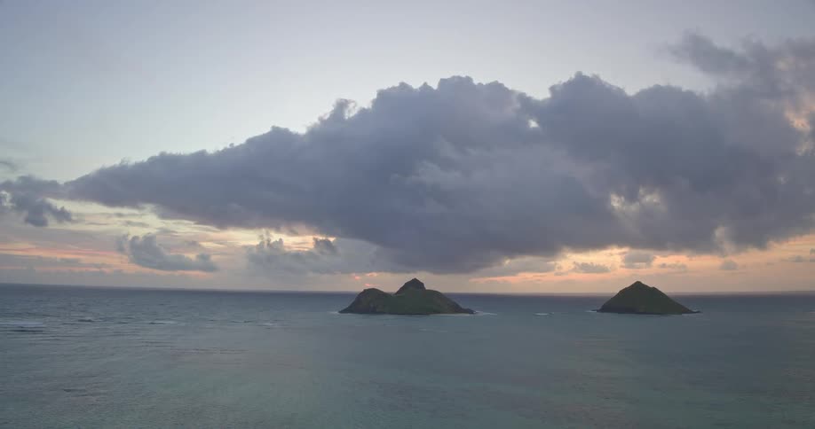 A serene, static wide shot of two small islands in the ocean at sunrise under a large, dramatic cloud