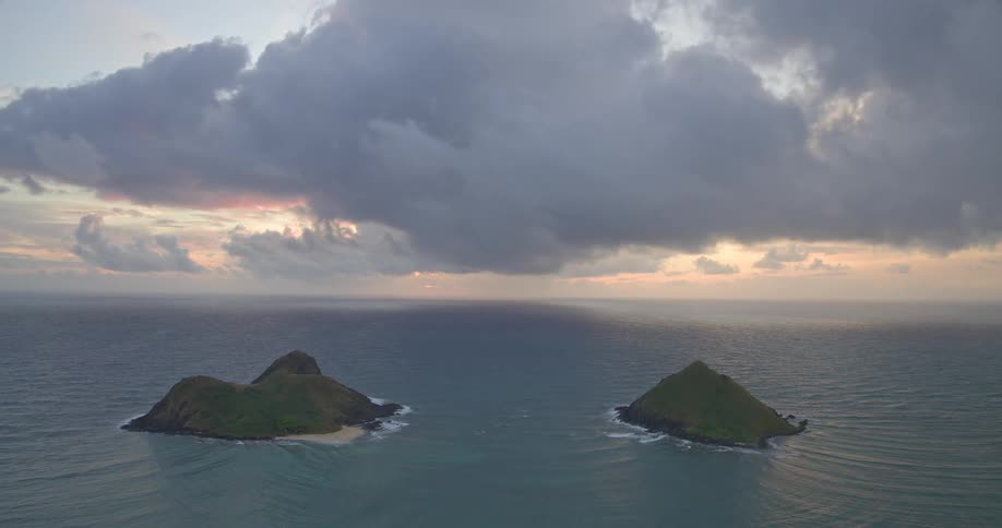 A serene and dramatic sunrise reveals two small tropical islands sitting in the vast ocean under a cloudy sky