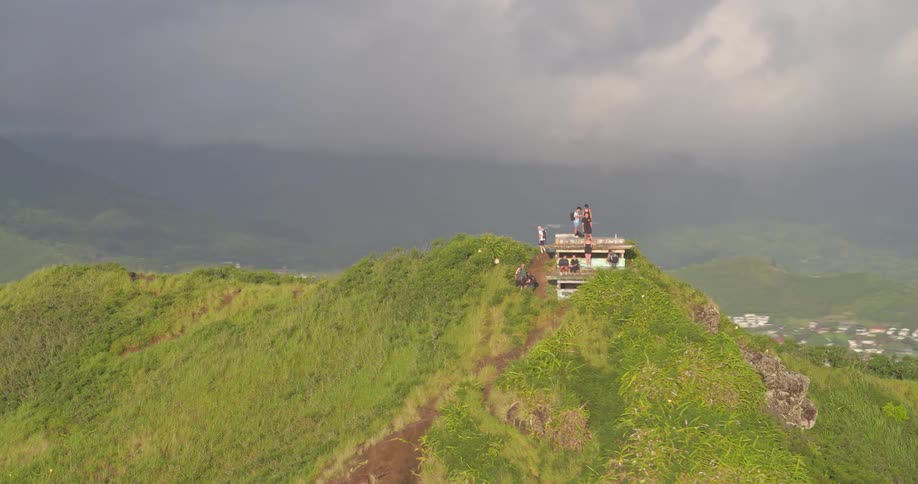 Epic aerial shot slowly approaches hikers at a scenic lookout point on a lush green mountain ridge