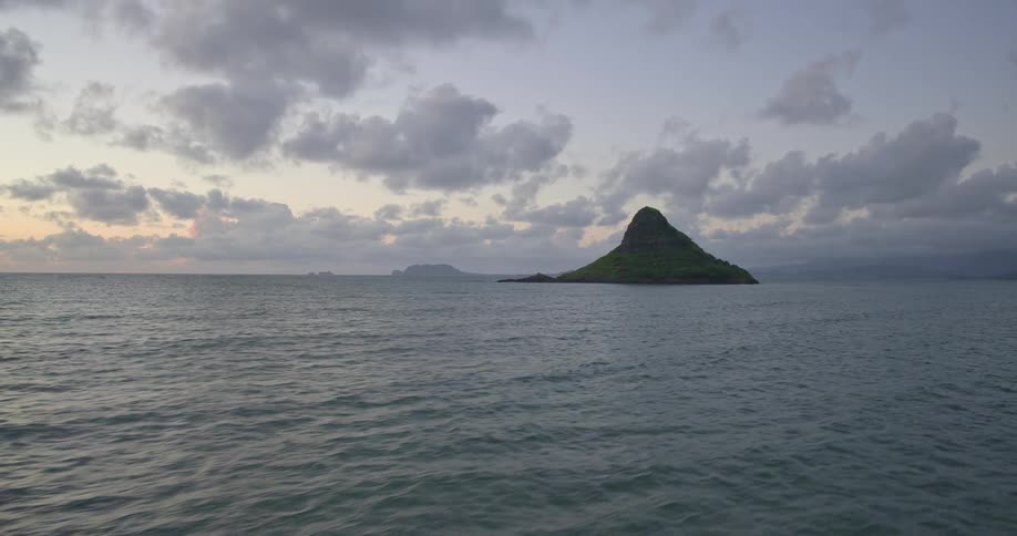 A serene view of the iconic Mokolii island, also known as Chinaman's Hat, in the ocean off Oahu, Hawaii at dusk