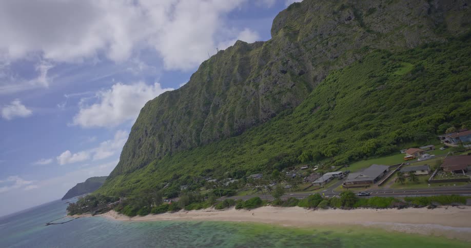 A stunning aerial view captures the dramatic green mountains meeting the turquoise Pacific Ocean along a picturesque Hawaiian coastline
