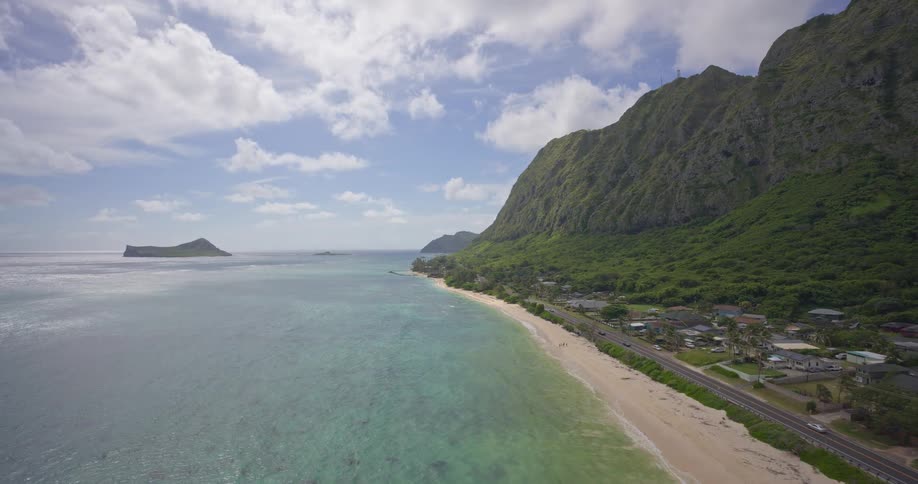 A breathtaking aerial view of a tropical Hawaiian coastline featuring lush green mountains, a sandy beach, and crystal-clear turquoise ocean
