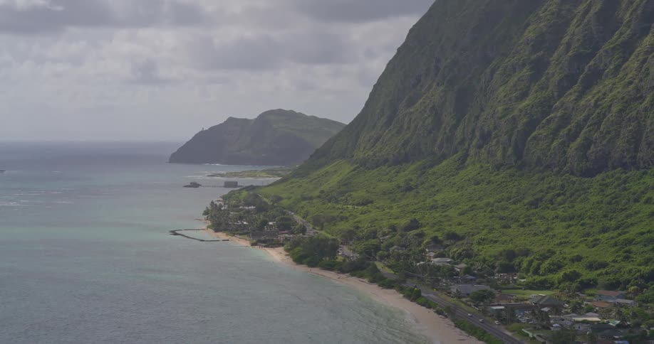 An aerial drone slowly ascends revealing the majestic and lush green mountain coastline of Hawaii on an overcast day