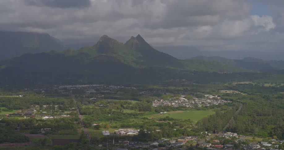 Sunlight breaks through dramatic clouds, illuminating a lush green valley and town nestled at the foot of majestic mountains