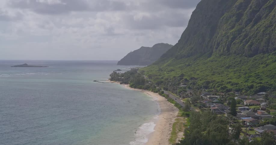A breathtaking high-angle view of a tropical Hawaiian coastline, featuring a sandy beach, a coastal town, and majestic green mountains