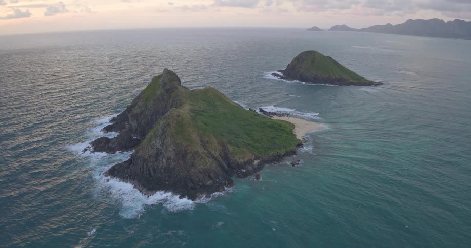 A stunning aerial wide shot of the iconic Mokulua Islands surrounded by the turquoise Pacific Ocean off the coast of Oahu, Hawaii at sunrise