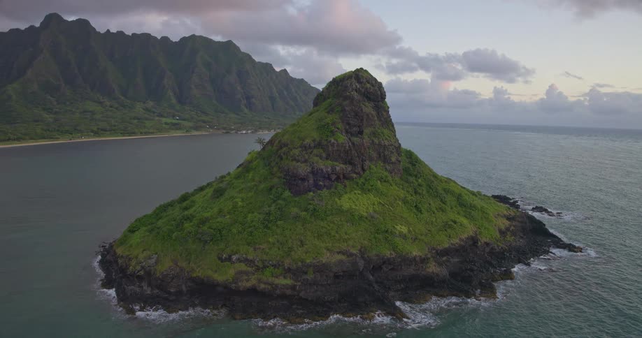 A stunning aerial view ascends over the verdant Mokoliʻi island, known as Chinaman's Hat, set against the majestic Koolau Mountains of Oahu at dawn