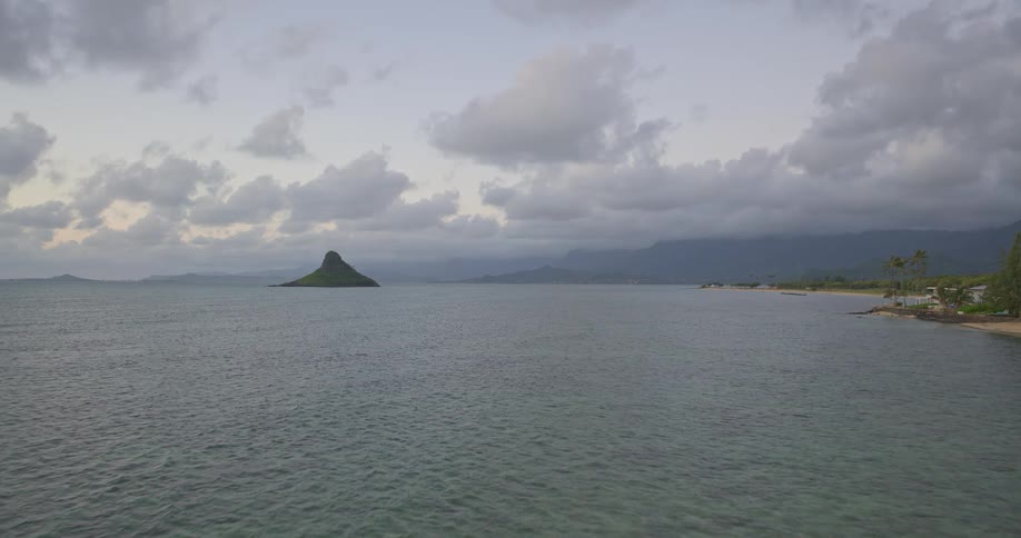 A tranquil wide shot of the iconic Mokolii Island, or Chinaman's Hat, off the coast of Oahu, Hawaii, during a cloudy twilight