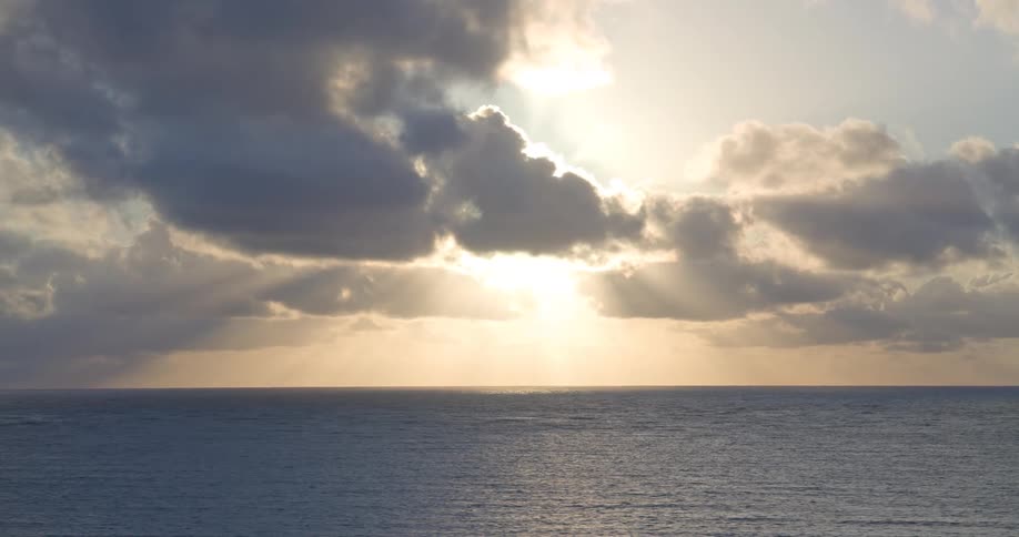 Majestic sunbeams radiate through a dramatic, cloudy sky over the vast, calm ocean